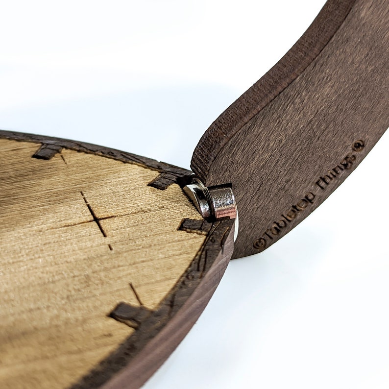 May include: Close-up of a wooden box with a hinged lid. The lid is open and the hinge is visible. The box is made of dark wood and has a light wood interior. The box is labelled "Tabletop Things".