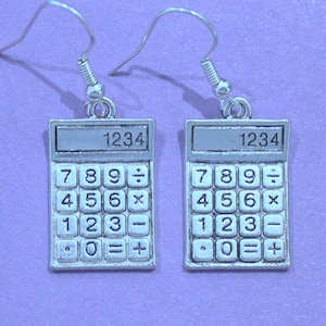 May include: Silver calculator earrings with a silver hook. The calculator face has the numbers 1234 at the top and the numbers 789, 456, 123, and 0 with the symbols -, =, x, and +.