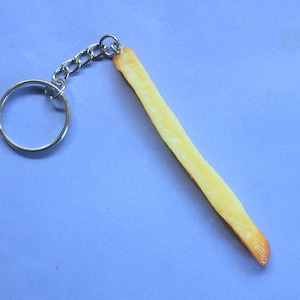 May include: A silver keyring with a realistic-looking french fry charm. The fry is yellow and brown and has a slight bend in it.