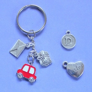 May include: A silver keyring with a red car charm, a silver envelope charm, a silver gift box charm, a silver heart charm with the word "sister" on it, and a silver charm with the letter "D" on it.