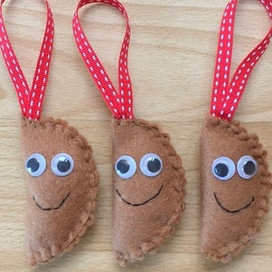May include: Three handmade felt ornaments shaped like smiling pastries, each with googly eyes and a stitched mouth. They are brown and attached to red and white ribbon loops for hanging.