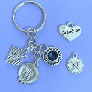 May include: Silver keyring with charms including a notepad with the word "memo" written on it, a plate with cutlery, a teacup, a heart charm with the word "Grandson" on it, and a circle charm with the letter "N" on it.
