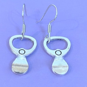 May include: A pair of silver bottle opener earrings. The earrings are shaped like a bottle opener with a small circle in the centre. The earrings are hanging from silver hooks.