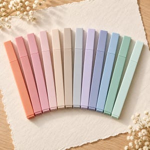 May include: A set of twelve rectangular markers arranged in a fan shape, featuring a gradient of colors including coral, pink, peach, beige, grey, lavender, periwinkle, blue, and mint green, each with a matching cap and a flat, smooth finish.