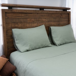 May include: A sage green linen bed sheet set with two matching pillowcases. The bed has a rustic wooden headboard with a metal accent.