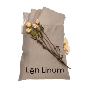 May include: A beige linen bag with a drawstring closure. The bag is filled with folded linen fabric and has the text "L&euml;n Linum" printed on the front. Dried flowers and leaves are placed on top of the bag.
