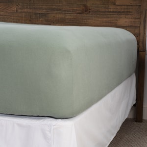 May include: A sage green fitted sheet with a white bed skirt. The sheet is made of a soft, breathable fabric and is perfect for a comfortable night's sleep.