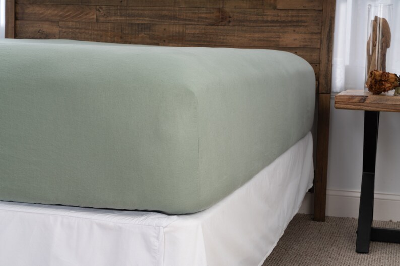 May include: A sage green fitted sheet with a white bed skirt. The sheet is made of a soft, breathable fabric and is perfect for a comfortable night's sleep.