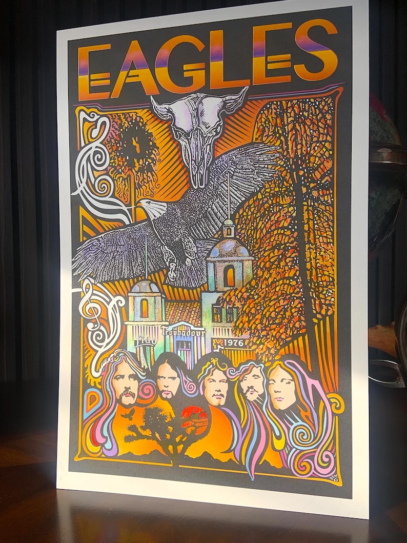 May include: A rectangular poster featuring the word EAGLES in orange and purple gradient text at the top. The artwork displays a white steer skull, a large eagle in flight, a building labeled Troubadour 1976, and five stylized portraits.