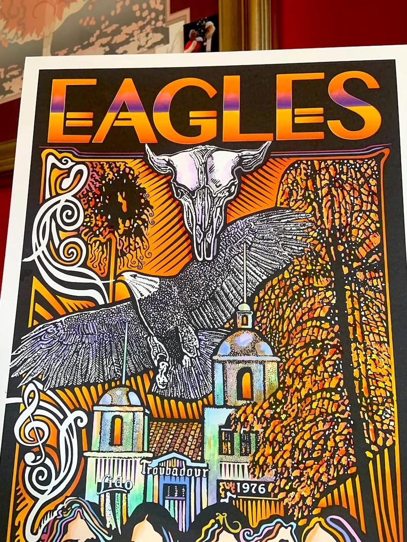 May include: A rectangular concert poster featuring the word EAGLES in a gradient orange and purple font. The artwork displays a central eagle in flight, a steer skull, a building labeled Troubadour 1976, and swirling white musical notes.