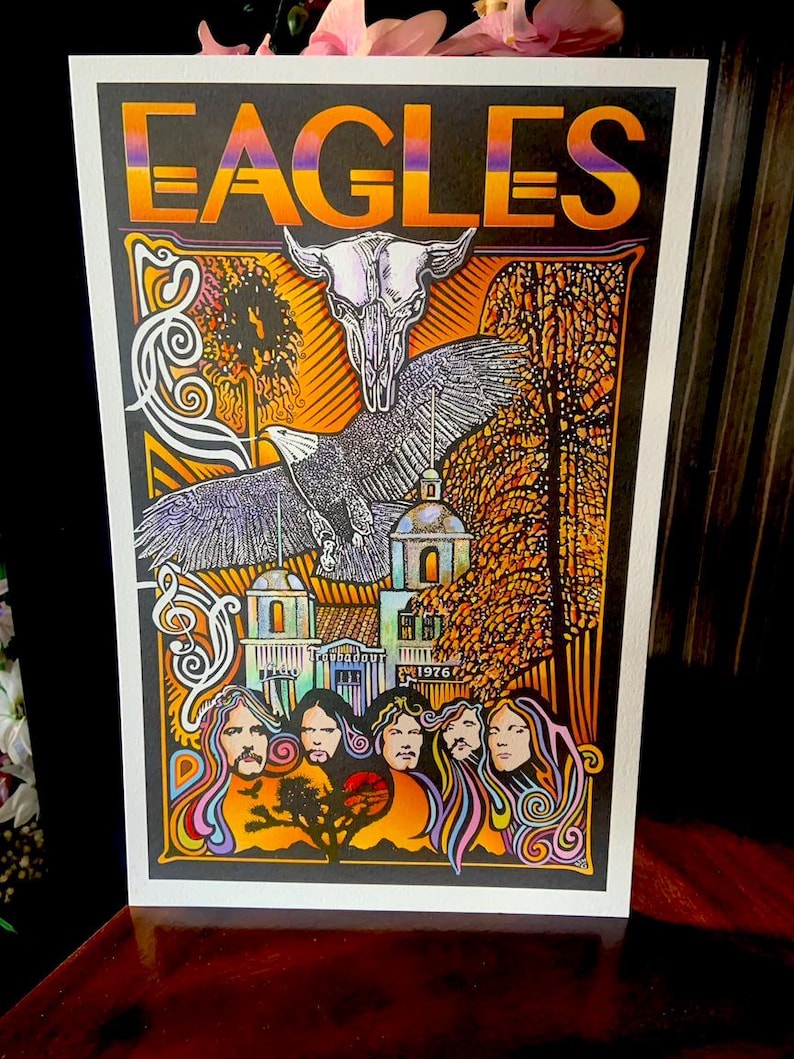 May include: A rectangular poster featuring the word EAGLES in orange and purple gradient lettering. The artwork displays a white animal skull, a flying eagle, a building labeled Troubadour 1976, and five stylized portraits with flowing hair.