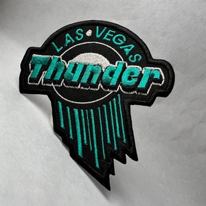 May include: Black and teal embroidered patch with the text "Las Vegas Thunder" in a circle with teal vertical lines below.
