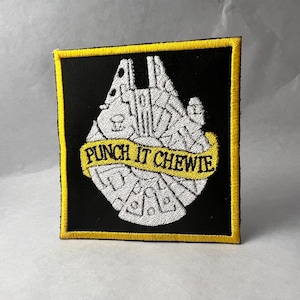 May include: A black and yellow embroidered patch featuring a white outline of the Millennium Falcon spaceship with the text "Punch It Chewie" on a yellow banner.