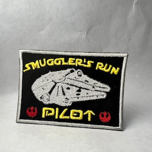 May include: A black embroidered patch with a white spaceship, yellow text that reads "Smuggler's Run Pilot", and red Rebel Alliance symbols.
