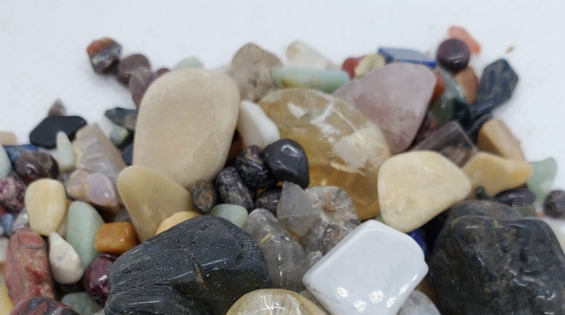 Pode incluir: Uma cole&ccedil;&atilde;o de pedras polidas de v&aacute;rios tamanhos e cores, incluindo branco, cinza, marrom, preto e transparente. As pedras est&atilde;o dispostas em uma pilha sobre uma superf&iacute;cie branca.