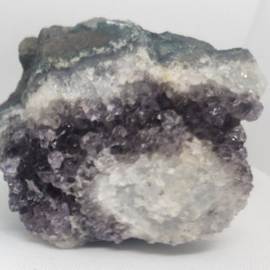 Pode incluir: Uma grande geoda de ametista com uma forma&ccedil;&atilde;o de cristais roxos e brancos. A geode tem um exterior &aacute;spero e natural e um interior liso e polido.