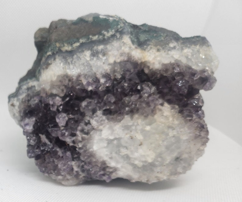 Pode incluir: Uma grande geoda de ametista com uma forma&ccedil;&atilde;o de cristais roxos e brancos. A geode tem um exterior &aacute;spero e natural e um interior liso e polido.