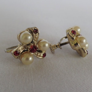 May include: A pair of gold tone clip-on earrings with faux pearls and red rhinestones.
