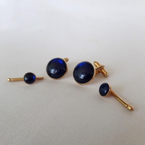 May include: A set of three gold cufflinks and a tie tack with blue glass stones.