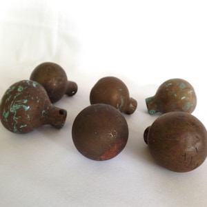 May include: Six round, brown metal knobs with a green patina. Some of the knobs have a more pronounced green patina than others.