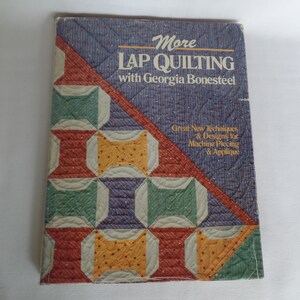 May include: Book cover with a purple, blue, and white striped background. The title is "More Lap Quilting with Georgia Bonesteel". The cover features a colorful quilt design with red, green, yellow, and white squares.