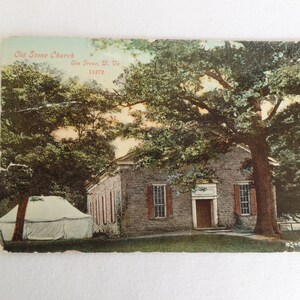 May include: A vintage postcard showing the Old Stone Church in Slm. Grove, W. Va. 11372. The church is a stone building with a wooden door and windows. The church is surrounded by trees and a white tent.