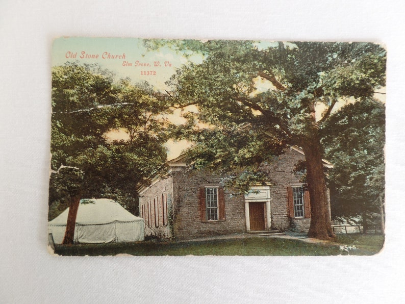 May include: A vintage postcard showing the Old Stone Church in Slm. Grove, W. Va. 11372. The church is a stone building with a wooden door and windows. The church is surrounded by trees and a white tent.