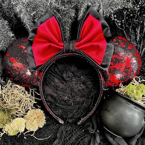 May include: Black and red mouse ears with a large red satin bow. The ears have a splatter paint design.