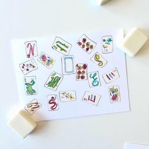May include: A collection of illustrated cards with various designs and numbers, scattered on a white surface. The cards feature colorful drawings of flowers, dragons, and other symbols. Several white square blocks are also present.