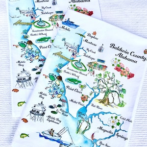 May include: Three white tea towels with a watercolor illustration of a map of Baldwin County, Alabama. The map includes various landmarks, including Mobile Bay, Fairhope, and Magnolia Springs. The text "Baldwin County, Alabama" is written in black at the top of each towel.
