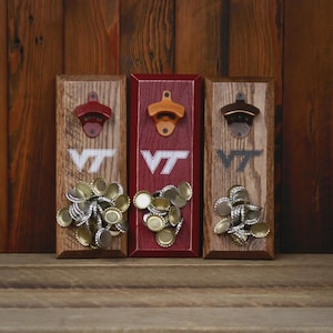 May include: Three wooden bottle openers with the letters "VT" and attached bottle caps. The openers are mounted on rectangular wooden plaques with different finishes: natural, red, and stained. Each opener has a different metal finish.