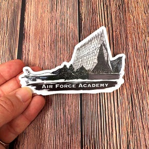 May include: A white sticker with a black and white illustration of the Air Force Academy Chapel. The text "AIR FORCE ACADEMY" is printed in black below the illustration.