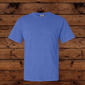 May include: A solid blue short-sleeved t-shirt. The shirt is made of a soft material and has a crew neck. The shirt is displayed on a wooden background.