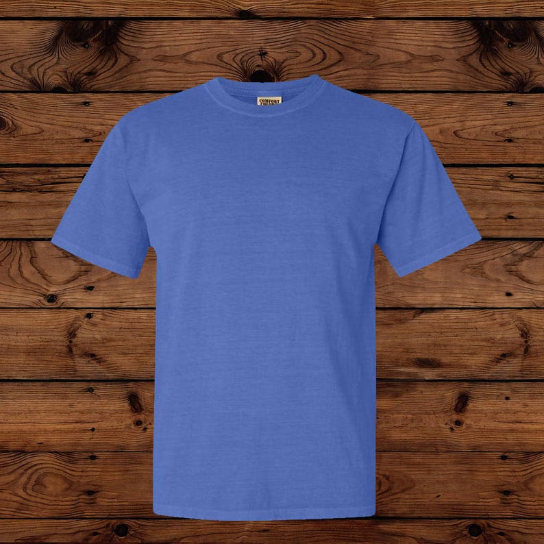 May include: A solid blue short-sleeved t-shirt. The shirt is made of a soft material and has a crew neck. The shirt is displayed on a wooden background.