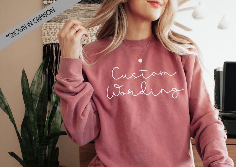 May include: A pink sweatshirt with the text "Custom Wording" in white script font.