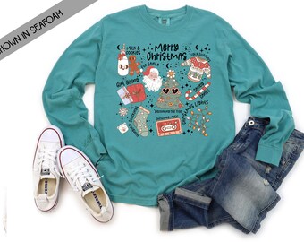 May include: A teal long-sleeved t-shirt with a Christmas-themed graphic featuring a Christmas tree, Santa Claus, gifts, candy canes, and the text "Merry Christmas".