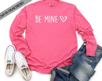 May include: Pink long-sleeve t-shirt with the text "BE MINE" and a white heart.