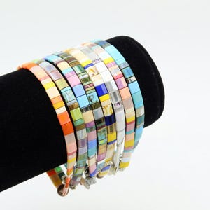 May include: A stack of colorful tile bracelets with various patterns and colors, including blue, green, yellow, pink, and orange.
