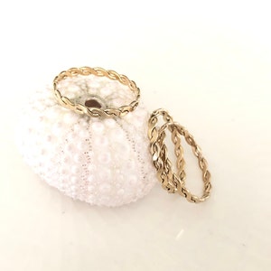 Op de afbeelding: Drie gouden gevlochten ringen op een witte zee-egel. De ringen zijn op elkaar gestapeld.