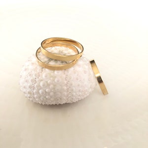 Op de afbeelding: Drie gouden ringen gestapeld op een witte zee-egel. De ringen zijn eenvoudig en hebben een gepolijste afwerking.