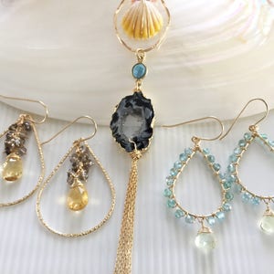 Peut inclure: Trois paires de boucles d'oreilles en or avec des accents de pierres précieuses. La première paire présente une forme de larme avec une pierre précieuse jaune et des pierres précieuses brunes. La deuxième paire présente une forme de larme avec une pierre précieuse bleue et une agate noire. La troisième paire présente une forme de larme avec une pierre précieuse bleue et une pierre précieuse verte.