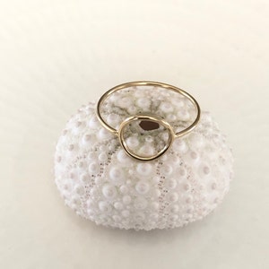 Op de afbeelding: Een gouden ring met een cirkelvormig ontwerp. De ring ligt op een witte zee-egel.