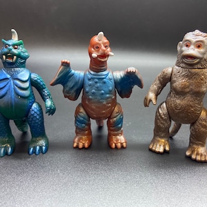 May include: Three toy monsters, a blue and green dinosaur, a brown and blue dinosaur with wings, and a brown monkey.