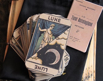 May include: A deck of tarot cards with a black bag and a small booklet titled "Tarot Astrologique Methode" by Georges Muchery. The top card shows a woman standing in front of a blue curtain with a crescent moon in the sky. The card is labelled "LUNE" in French.