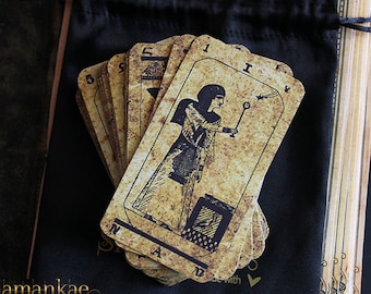 May include: A deck of tarot cards with an Egyptian theme. The cards are in a black velvet bag and feature an illustration of a woman holding a wand. The card in the front reads "I - The Magician".