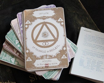 Op de afbeelding: Een set vintage tarotkaarten met een bruine en witte kaart bovenop met een cirkel met een driehoek erin en de tekst "7e TRIANGLE DU SOLEIL. ACCORD de Maria ou autre." De kaarten zijn in een waaier geordend en hebben verschillende kleuren en ontwerpen.
