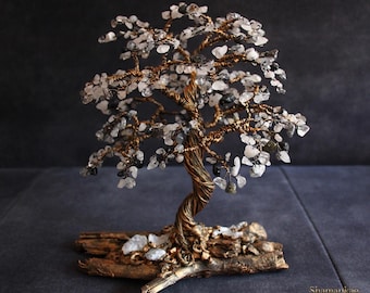 May include: A handcrafted decorative tree sculpture with a twisted copper wire trunk and branches. The branches are adorned with small, clear and gray gemstones, resembling leaves. The tree is mounted on a piece of natural wood.