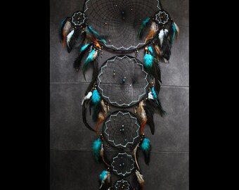 May include: A multi-hoop dreamcatcher with a black web design, adorned with turquoise, brown, and black feathers. The dreamcatcher has a series of circular and star-shaped hoops, with beaded accents. The text "Shamankae" is visible at the bottom.