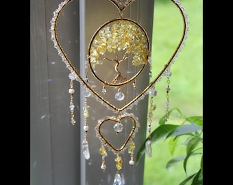 May include: A hanging ornament featuring a large gold wire heart frame lined with clear beads, enclosing a circular gold wire tree of life with yellow crystal leaves. A smaller gold heart hangs below, accented with clear and yellow crystal dangles.