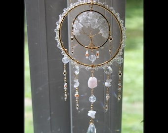 May include: A circular gold-toned wire suncatcher featuring a central wire-wrapped tree with white crystal leaves. The outer ring is adorned with clear beads, and multiple dangling strands feature clear crystals, pink stones, and gold accents.